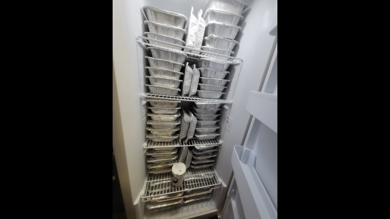 An upright deep freezer full of frozen meals in aluminum pans