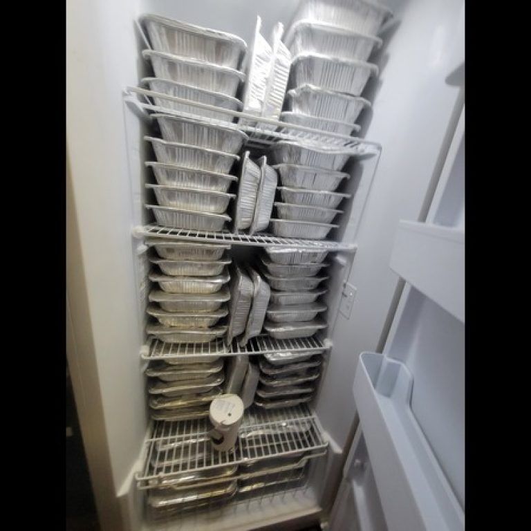 An upright deep freezer full of frozen meals in aluminum pans
